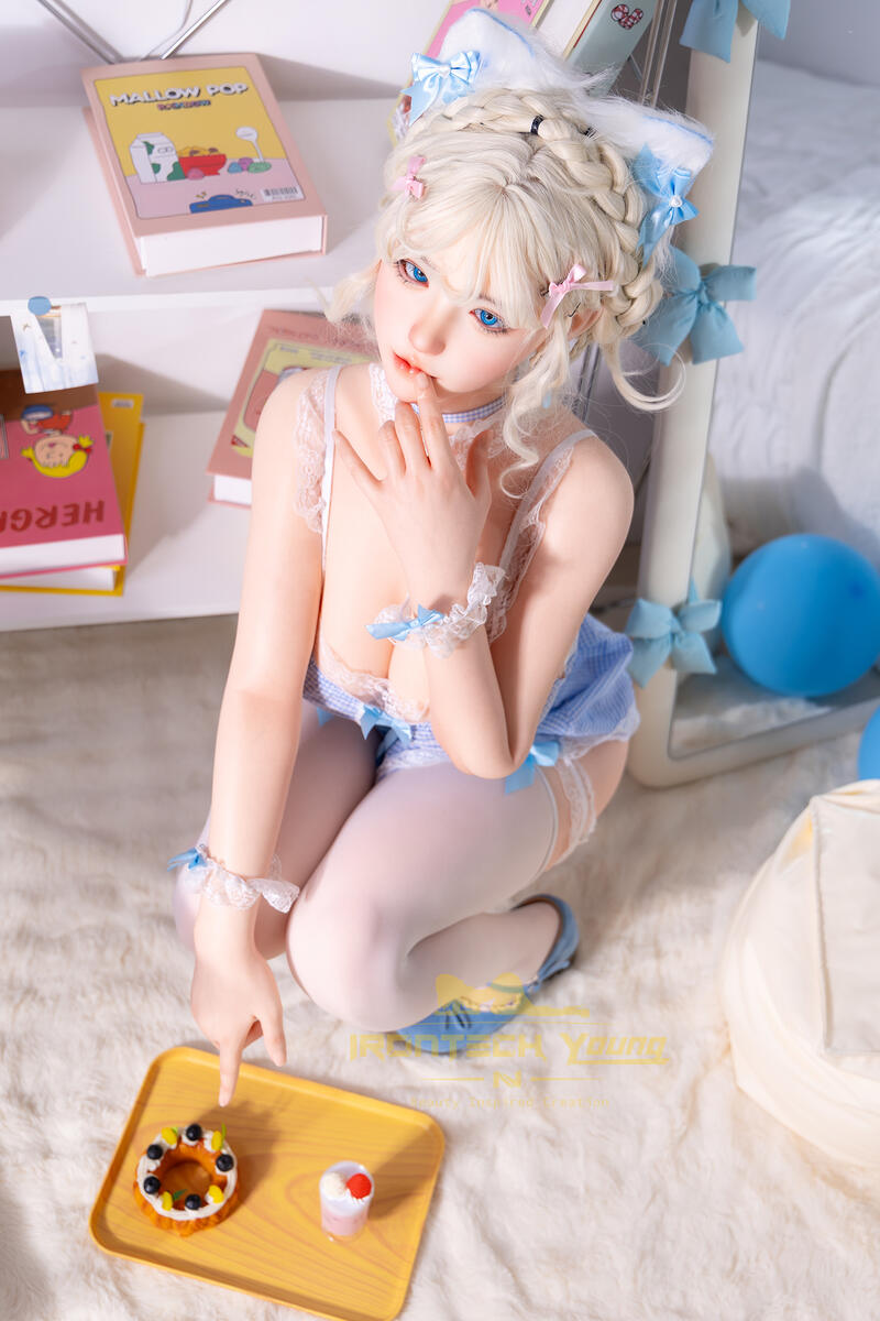 Irontech sexuelle doll Akiyama mit blauen Schleifen beim entspannten Sitzen im Schlafzimmer