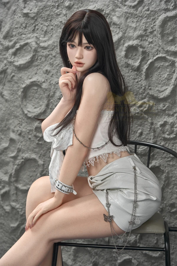 Premium Lovedoll Zuri stützt das Kinn auf die Hand und lächelt leicht, ein Moment stiller Nachdenklichkeit