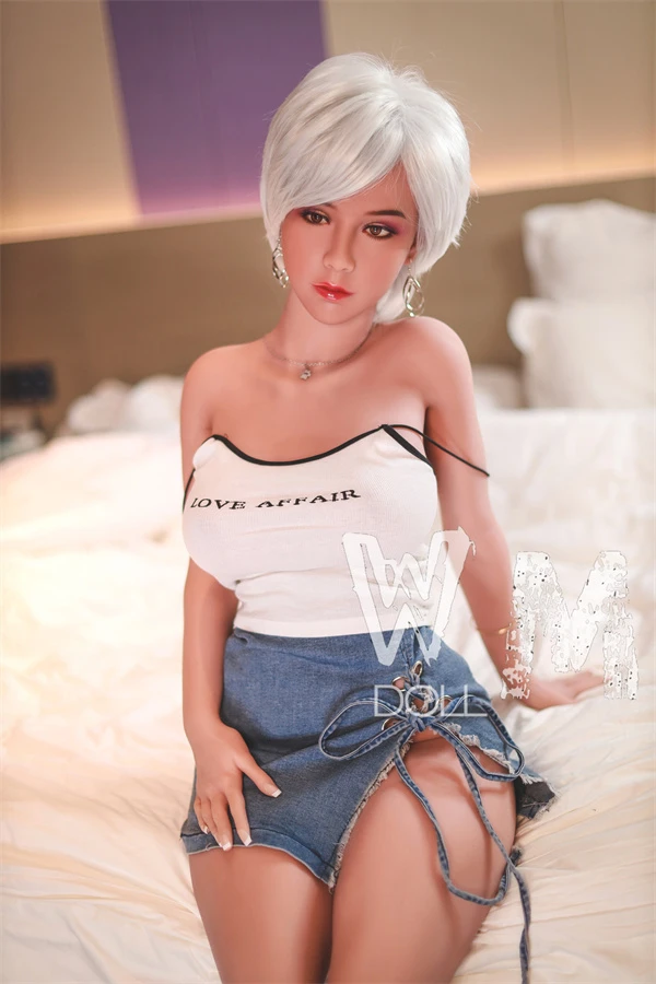 Realistische Liebespuppe in sexy Jeansrock sitzt auf dem Bett