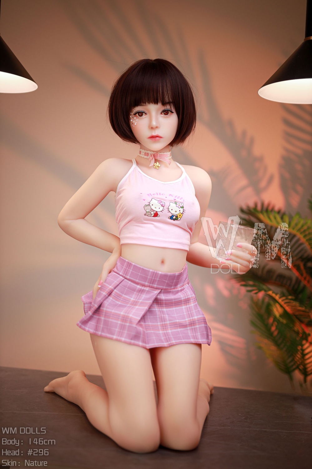 Real TPE Sexpuppe Zoey mit kurzem Bob, kniend auf Sofa in rosa Crop-Top und kariertem Minirock